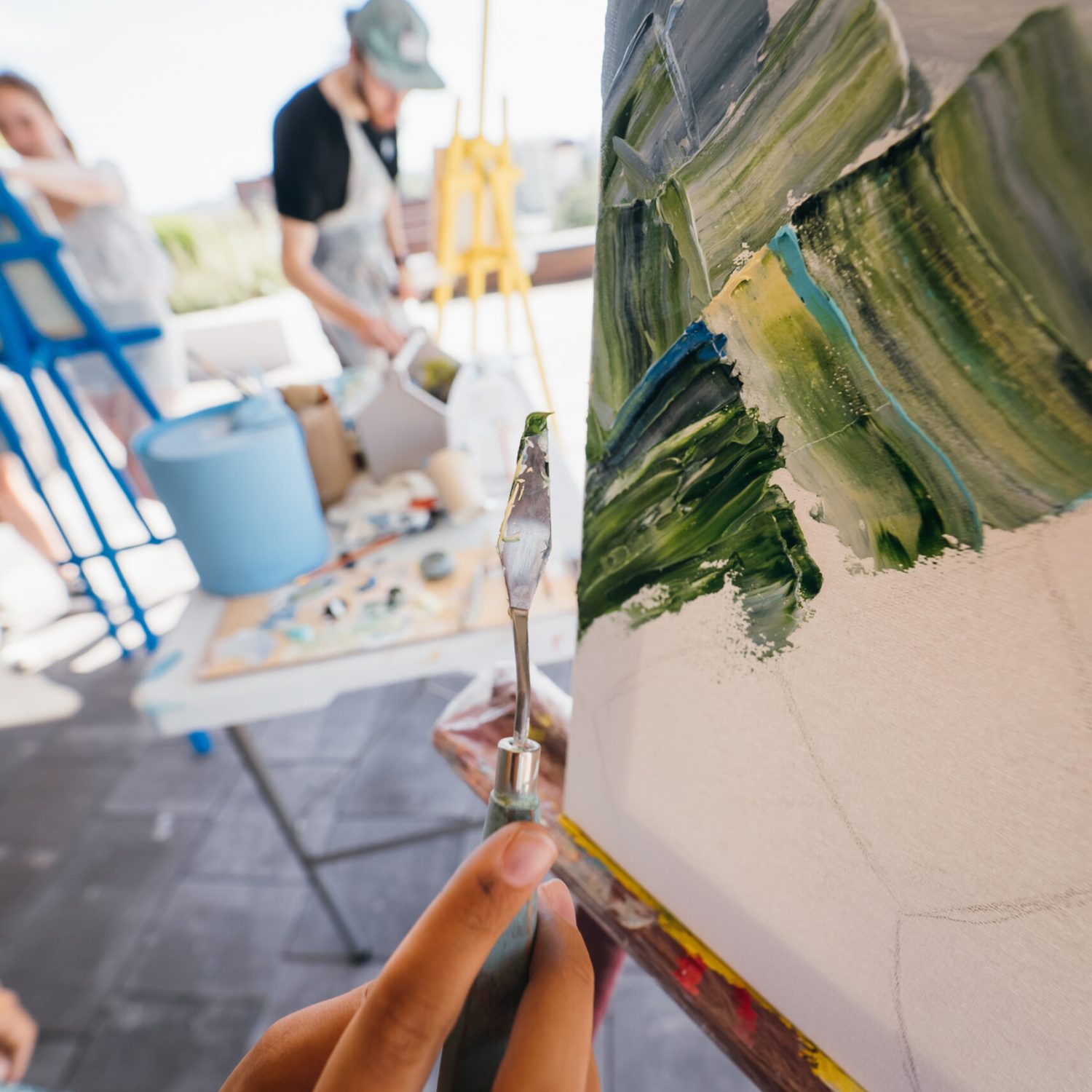 Close-up of a woman's hand applying paint to a canvas with a spatula